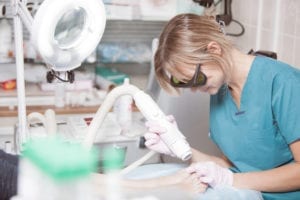 Female cosmetician in safety glasses at work. She providing a foot treatment with a laser